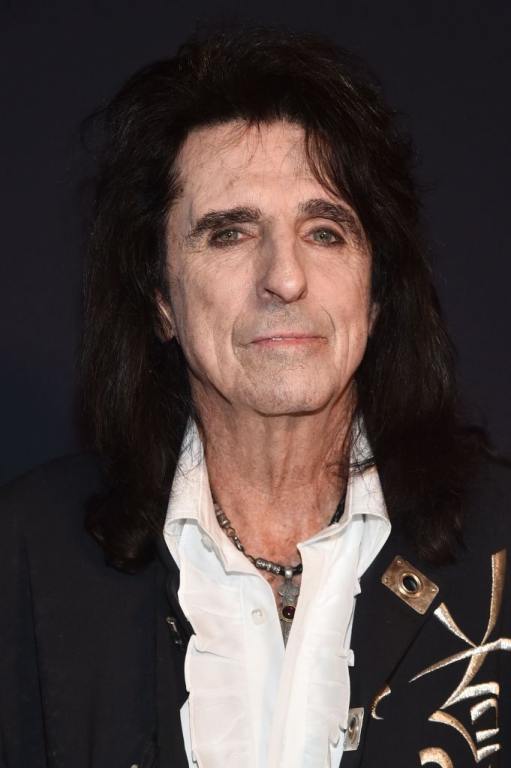 Alice Cooper attends the Pre-GRAMMY Gala & GRAMMY Salute to Industry Icons wearing eyeliner, his long dark hair worn down, a white ruffled collared shirt under a black jacket with gold embroidery and a skull necklace.