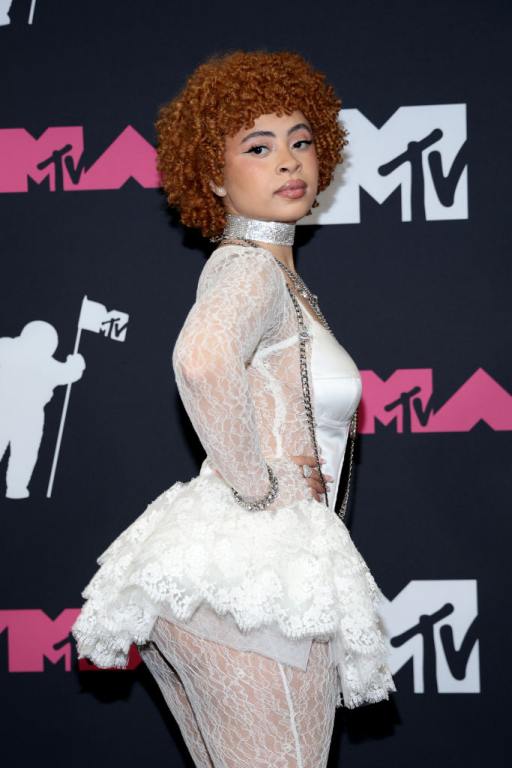 Ice Spice poses in the press room at the 2023 MTV Video Music Awards wearing a white minidress with white lace tights.