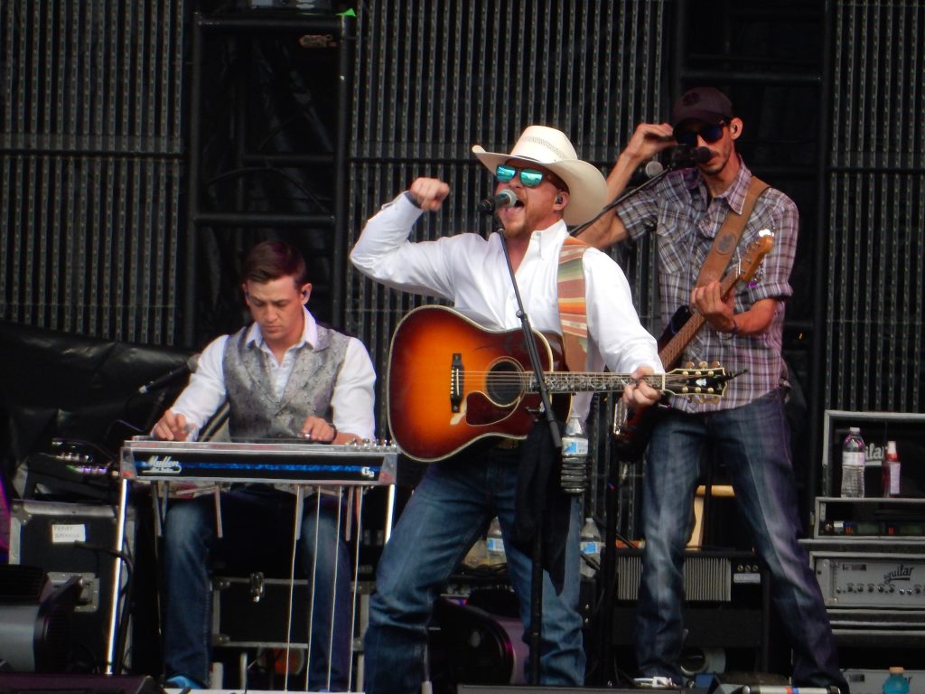 Cody Johnson in white cowboy hat, white shirt and jeans fist pumping on stage while holding a guitar while he plays Fenway Park in Boston, Ma.