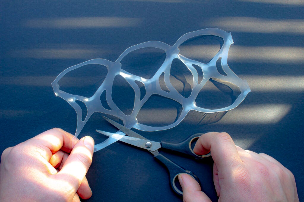 A person cutting a six pack rings or six pack yokes with scissors