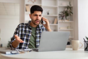 Confused man talking on mobile phone using laptop