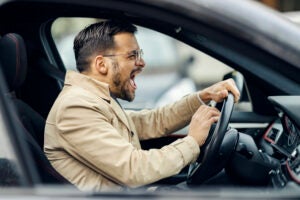 An angry trendy driver is honking on other drivers while sitting in a car.