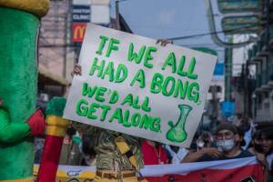 Person holding up a sign that reads "If we all had a bong, we'd all get along," with a hand drawn picture of a bong on it.