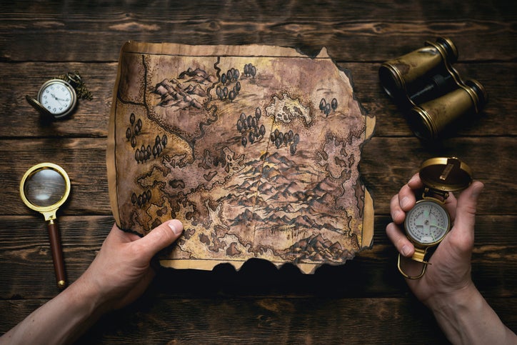 Old map in man adventurer hands on a brown table background. Treasure hunt map