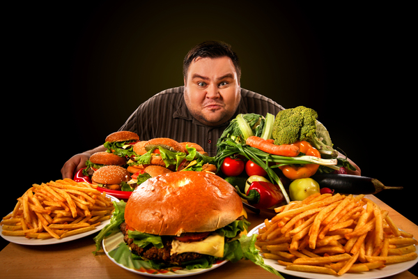 Fat man sitting in front of many types of unhealthy foods