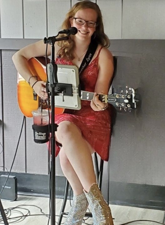 Heather Lynn sitting with guitar and microphone, smiling. 