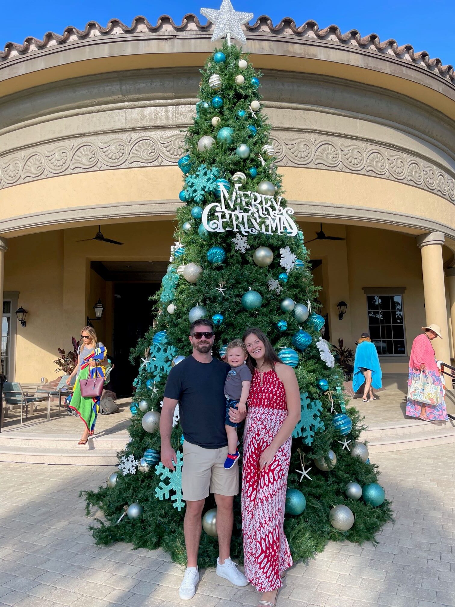 Ayla Brown, Rob Bellamy, and Barrett Bellamy standing in front of a Christmas tree in Naples. 