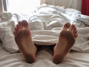 Dirty bare feet of a sleeping person showing out of the blanket on a bed. Hygiene or unsanitary conditions concept