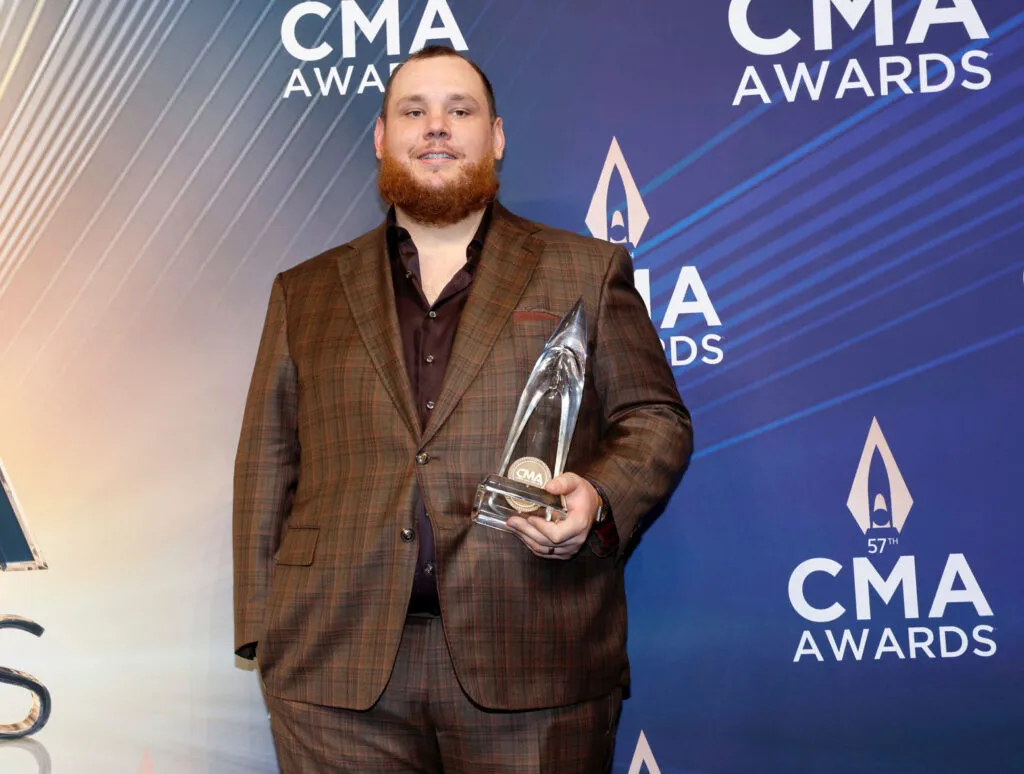 Luke Combs Teased Fans - Luke backstage, holding his 2023 CMA Award in a brown suit. 