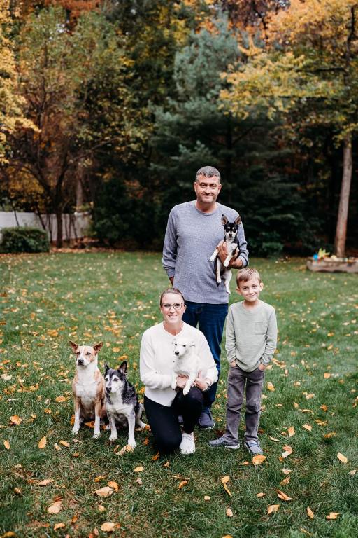 A picture of a wife, husband and 5 year old son posing outside with their four dogs.